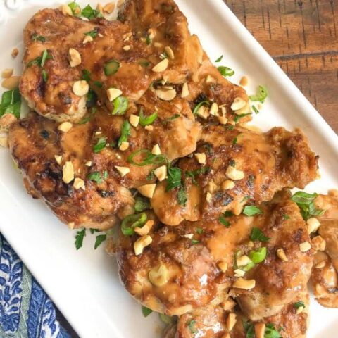 Thai Chicken Thighs on white platter garnished with green onion and chopped peanuts