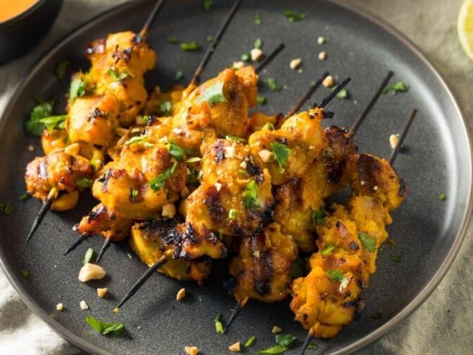 spicy chicken satay on a black plate on a wooden table