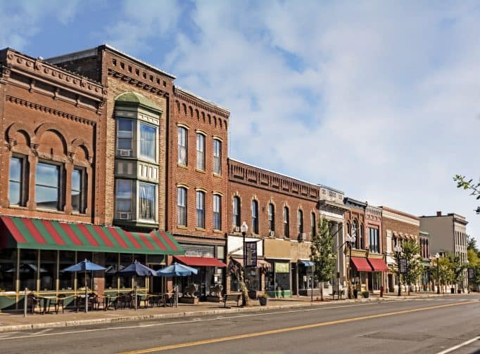A photo of a typical small town main street in the United States of America. Features old brick buildings with specialty shops and restaurants. Decorated with autumn decor. An idea for a staycation