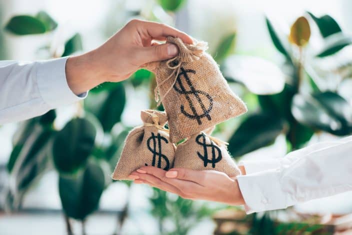 burlap sacks exchanging hands with money symbols on them. A representation of investing money for financial health