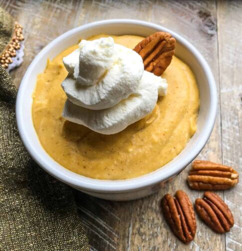 Pumpkin Mousse in a ramekin on a table topped with whipped cream and pecans