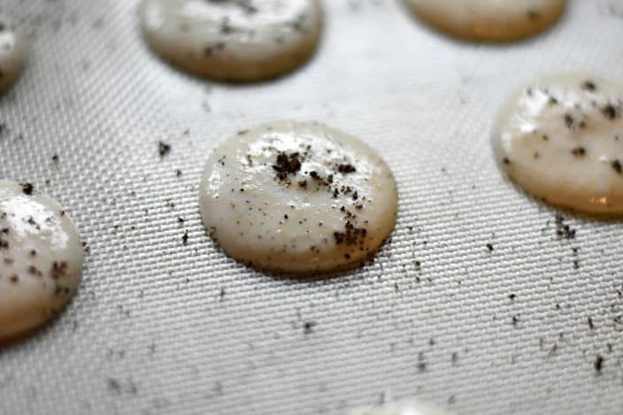 macaron mixture piped into circles to make macaron cookies with crushed Oreo pieces