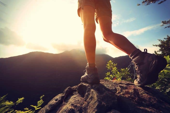 a female hiking in the mountains, view of her boots and legs, rocks and the sun shining bright