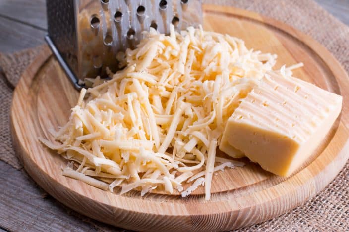 shredded cheese on a wooden board with a cheese grater