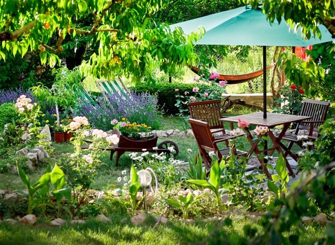 garden furniture with a teal umbrella and flowers and trees as part of creating shade in a backyard oasis