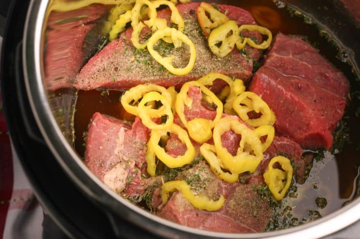 roast beef in a pot with banana peppers and spices to make italian beef