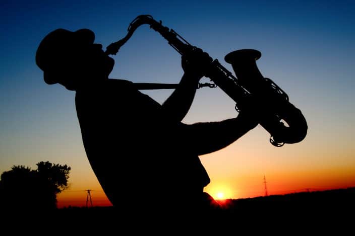 an outline of a blues player playing a saxophone in front of a sunset
