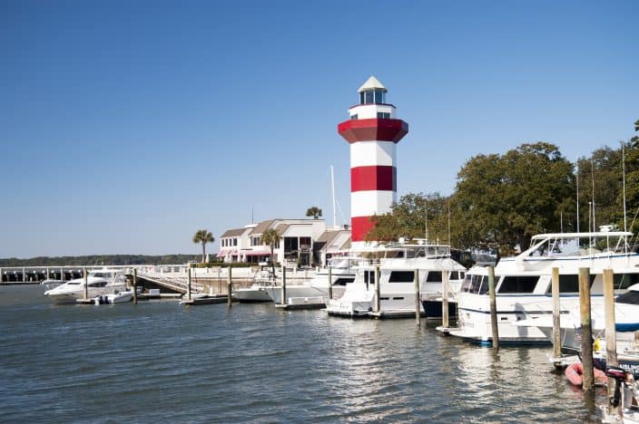 Harbour Town Lighthouse, Hilton Head Island, South Carolina with blue skies and waters and large boats. The perfect place for a romantic anniversary