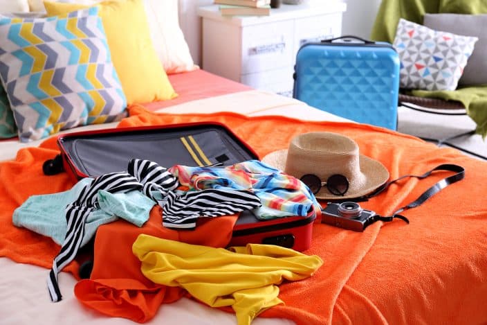 a suitcase packed for a traveling with sunglasses and a hat on an orange bed