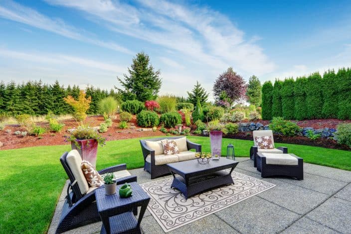 a backyard oasis with patio furniture, flowers and hedges