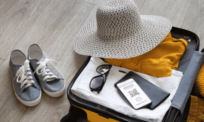gray tennis shoes with white laces and a hat laying on a suitcase with sun glasses, papers, and clothes