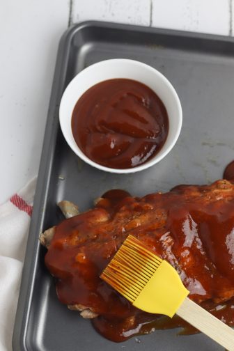 barbecue sauce painted on a rack of ribs with a bowl of sauce next to them