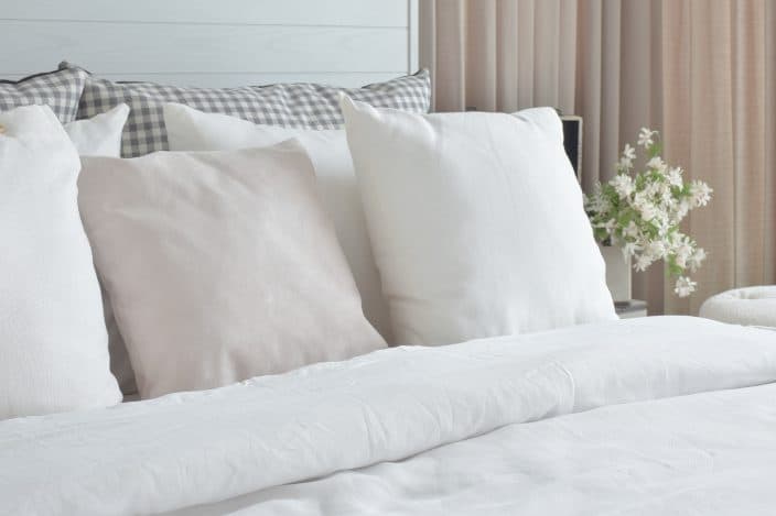 a clean made bed with white linens to represent changing bed sheets as part of your pre-travel to do list