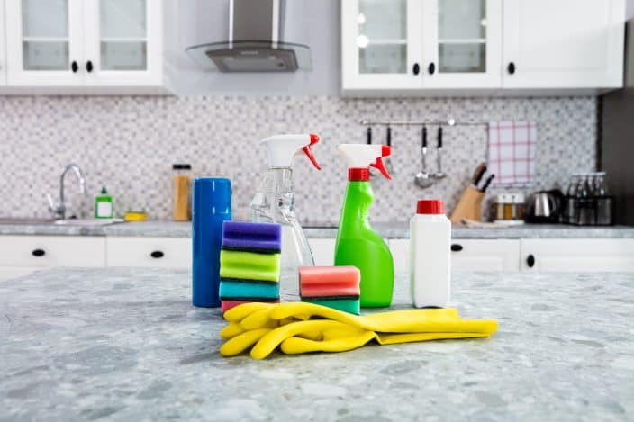 cleaning supplies on kitchen counter top to convey the importance of cleaning your kitchen before traveling