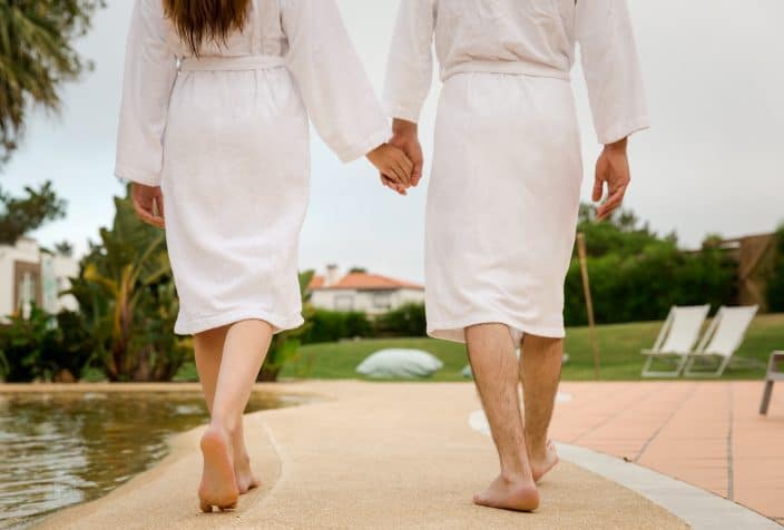 a couple in robes walking hand in hand by the pool