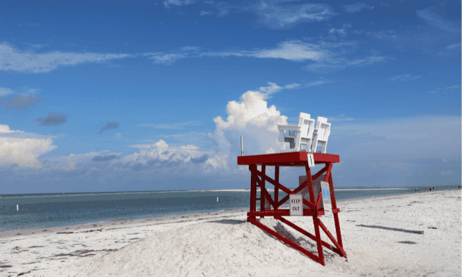 St. Petersburg Beach Dog friendly pet friendly beach with blue skies and white puffy clouds and a red lifeguard station overlooking the water with two white chairs on top.