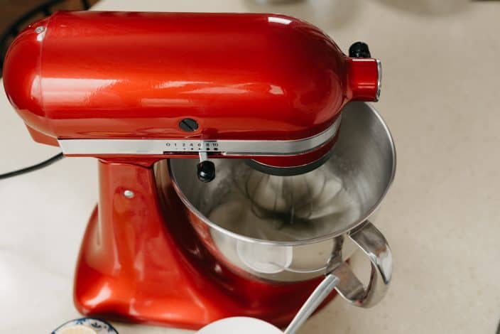 A close photo of a red stand mixer which is whipping the egg whites in a stainless steel bowl to make meringue for possum pie in a kitchen.
