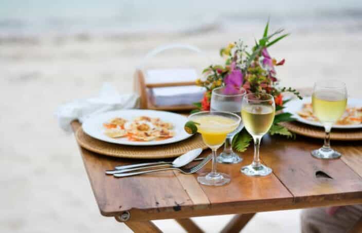 a wooden table on the beach with dinner and a glass of wine