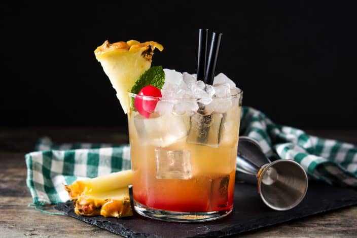 Easy mai tai cocktail with pineapple and cherry on wooden table.