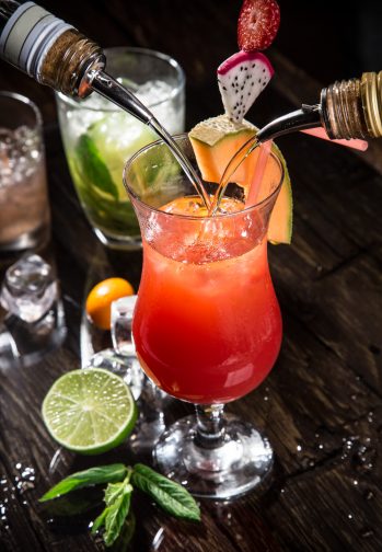 mai tai cocktail being made at a bar with lime and liqueurs being poured into the glass