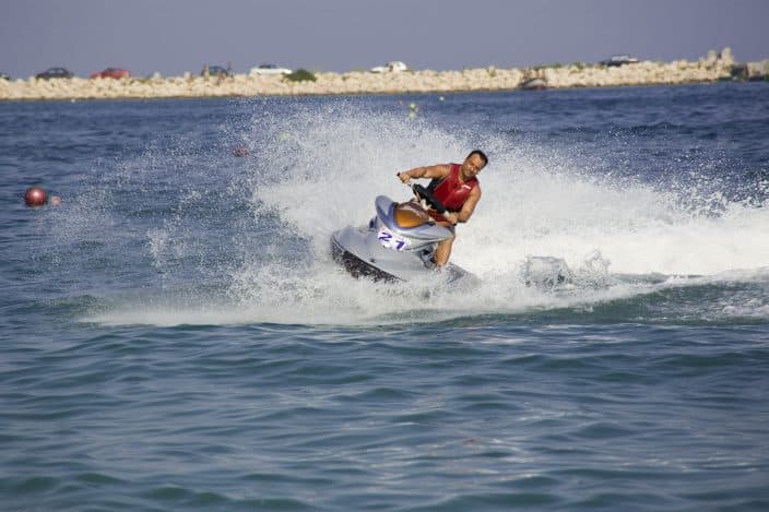 Man jet skiing in the sea leaving a splash of water behind as he moves fast, a fun beach day activity.