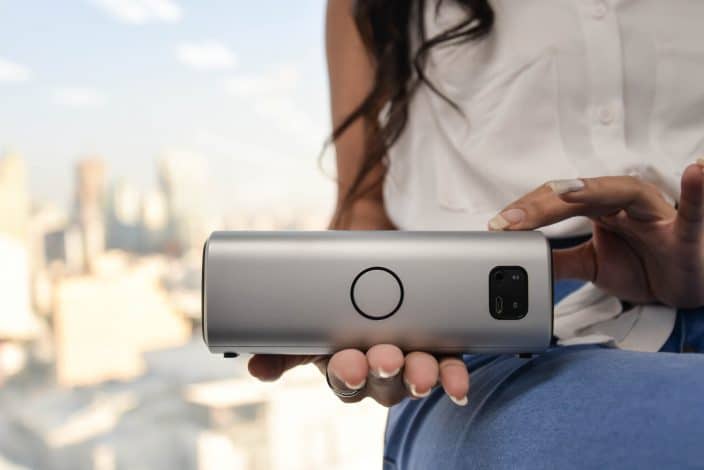 Women in a white shirt and blue jeans holding wireless speakers in her hand, to represent a beach day essential.