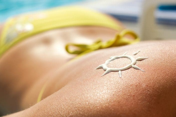 women laying under the sun face down with a sunscreen drawn sun on her back at the beach