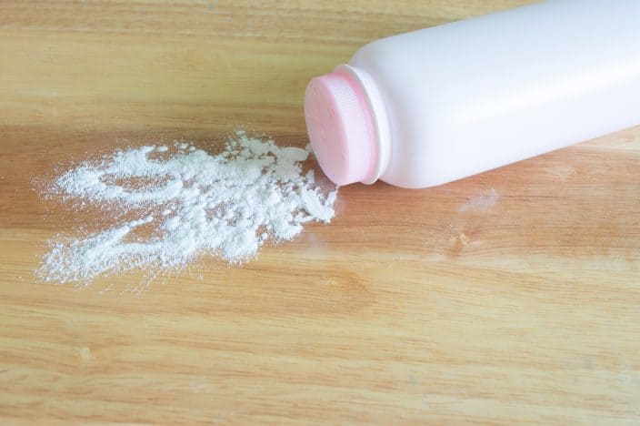 a bottle of baby powder with a pink top is laying on a wooden table with some powder falling out and spread on the table. 
