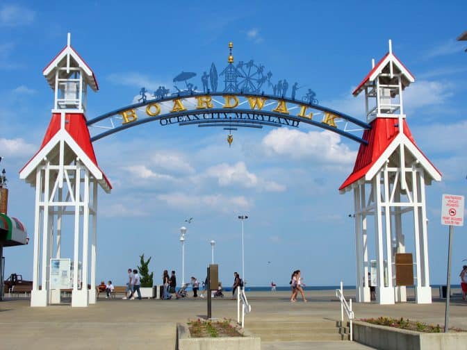 The famous public BOARDWALK sign located at the main entrance of the boardwalk with people walking in the background and blue skies in Ocean City, Maryland.
