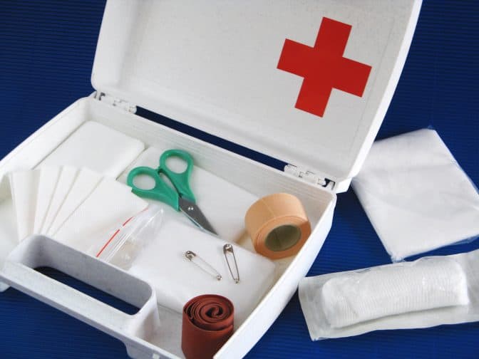 Picture of the first aid kit in a white box with bandages, wrapping tape, scissors inside, a camping essential.