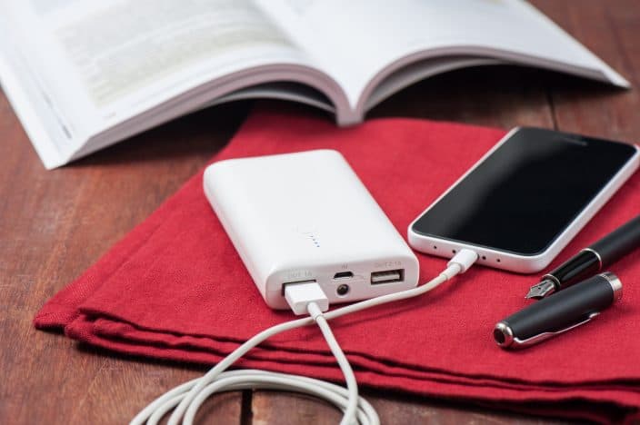 a white power bank connected to a white iPhone, laying on a red cloth napkin on a wooden table with a fountain pen and an open book