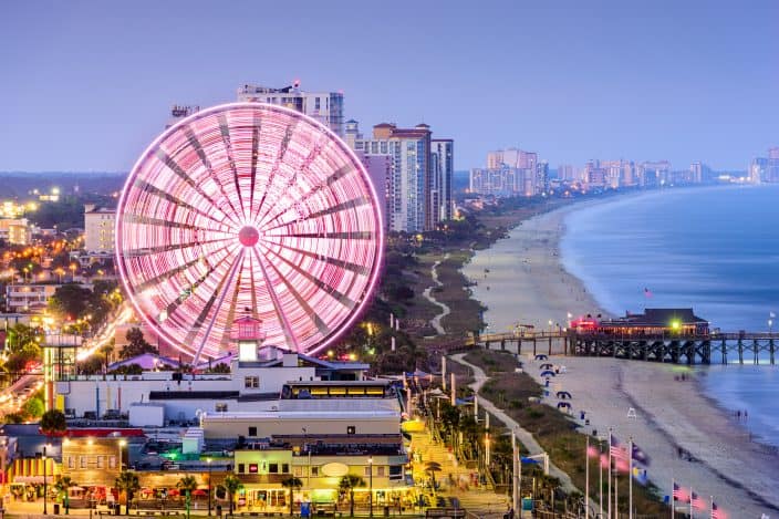 Myrtle Beach, South Carolina skyline along the beach at night with the ferris wheel and cityscape lit up with lights, a South Carolina romantic getaway idea.