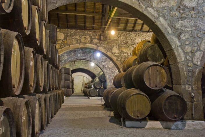 old cellar with rows of wooden wine barrels stacked on top of each other with grey arches made of stone in a Georgia Winery
