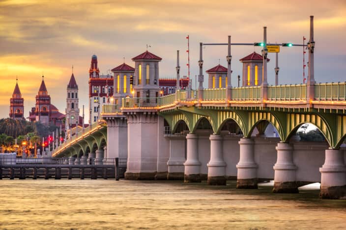 St. Augustine, Florida, USA city skyline and Bridge of Lions during sunset with orange and pink skies and golden water below the bridge, an example of what to see when staying at the St. Francis Inn .