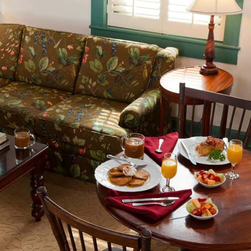 breakfast at the St. Francis Inn with pancakes, orange juice, coffee, and fruit on a wooden table with a flower sofa behind it.  