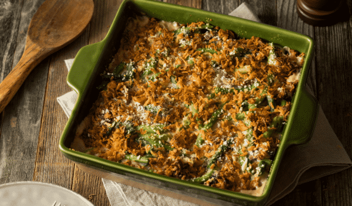 bacon green bean casserole in a green baking dish on a wooden table with a wooden spoon next to it 