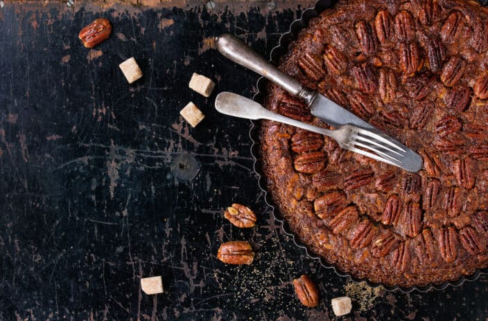 Homemade Big round maple pecan pie in black iron forms, served with brown sugar and vintage cutlery over old black wooden background. 