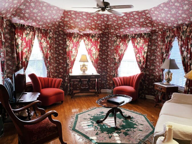 Heron Cay sitting room in Mount Dora with red arm chairs, floral accents, wooden floors, and a wall of windows with a Victorian Era vibe 