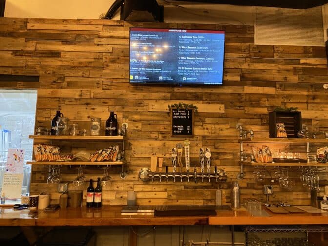 The wooden bar at Wolf Branch Brewing in Mt. Dora, Florida featuring various beer taps and a screen depicting the menu