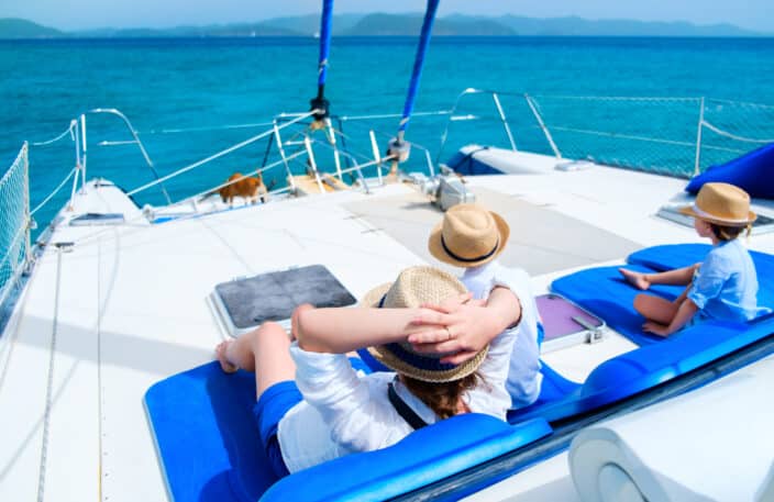Back view of a mother with a hat on, cruising with kids with hats on, relaxing having great time sailing on a luxury charter cruise yacht on a blue ocean with blue skies 