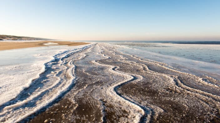 frozen beach view with sand and ice in water an example of things to do in winter