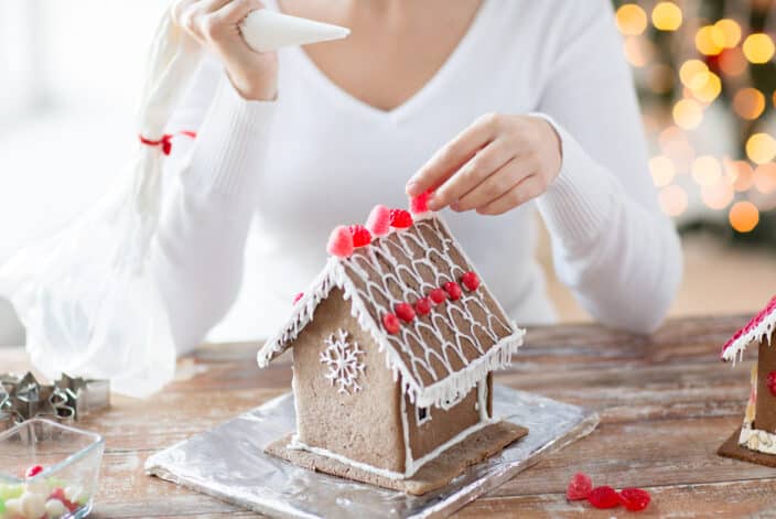 close up of a happy woman in a white sweater making gingerbread houses at home