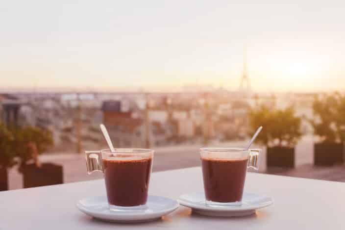 two cups of hot chocolate with the sunrise and city skyline in the background