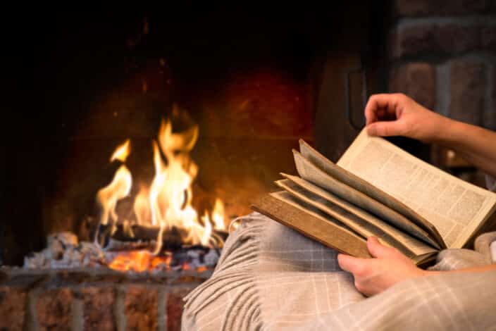 hands of woman reading book by fireplace an example of things to do in winter