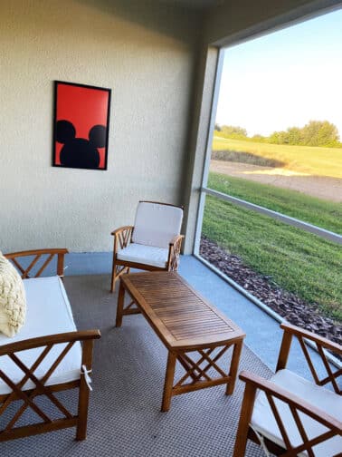 Outdoor patio with wooden furniture and a Mickey Mouse image on the wall overlooking a lake in a Kissimmee VHC rental home