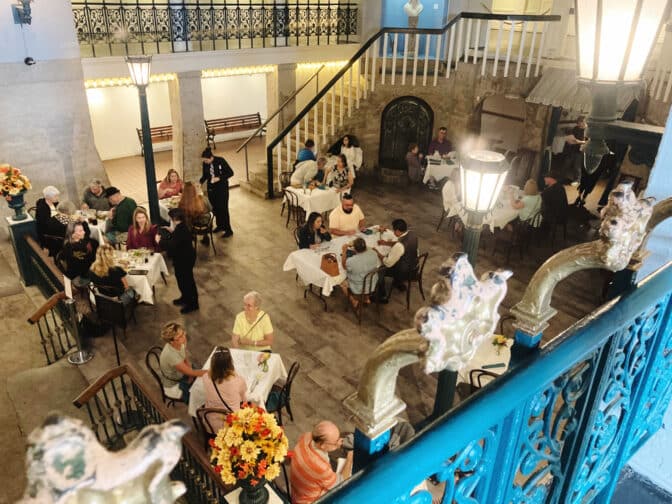 Alcazar Cafe in St Augustine with lots of people sitting at small tables with white tablecloths, wood floors, and blue accents