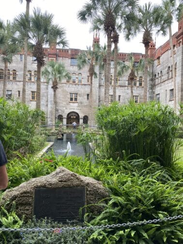 The outside of the Lightner Museum in St. Augustine with green grass, palm trees, and a water feature