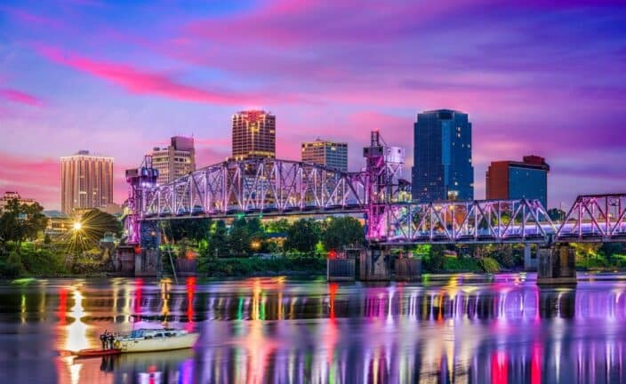 a city scape of Arkansas with a sunset skies made of pinks and purples, to represent an romantic getaway to Arkansas