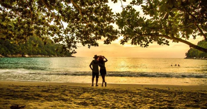 a couple on the beach under trees at sunset to represent a romantic getaway