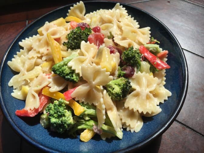 a close up of a broccoli pasta salad on a blue plate and wooden table
